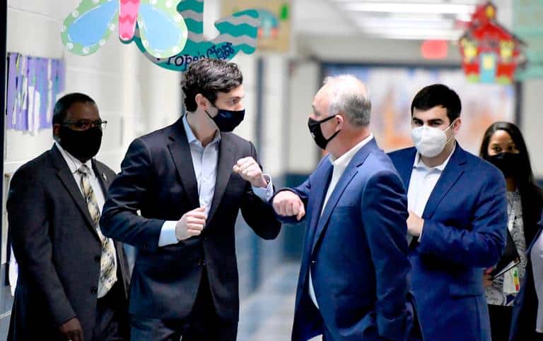 Senator Ossoff bumping elbows with someone in the hallway of a school with staffer Jake Best in the background.