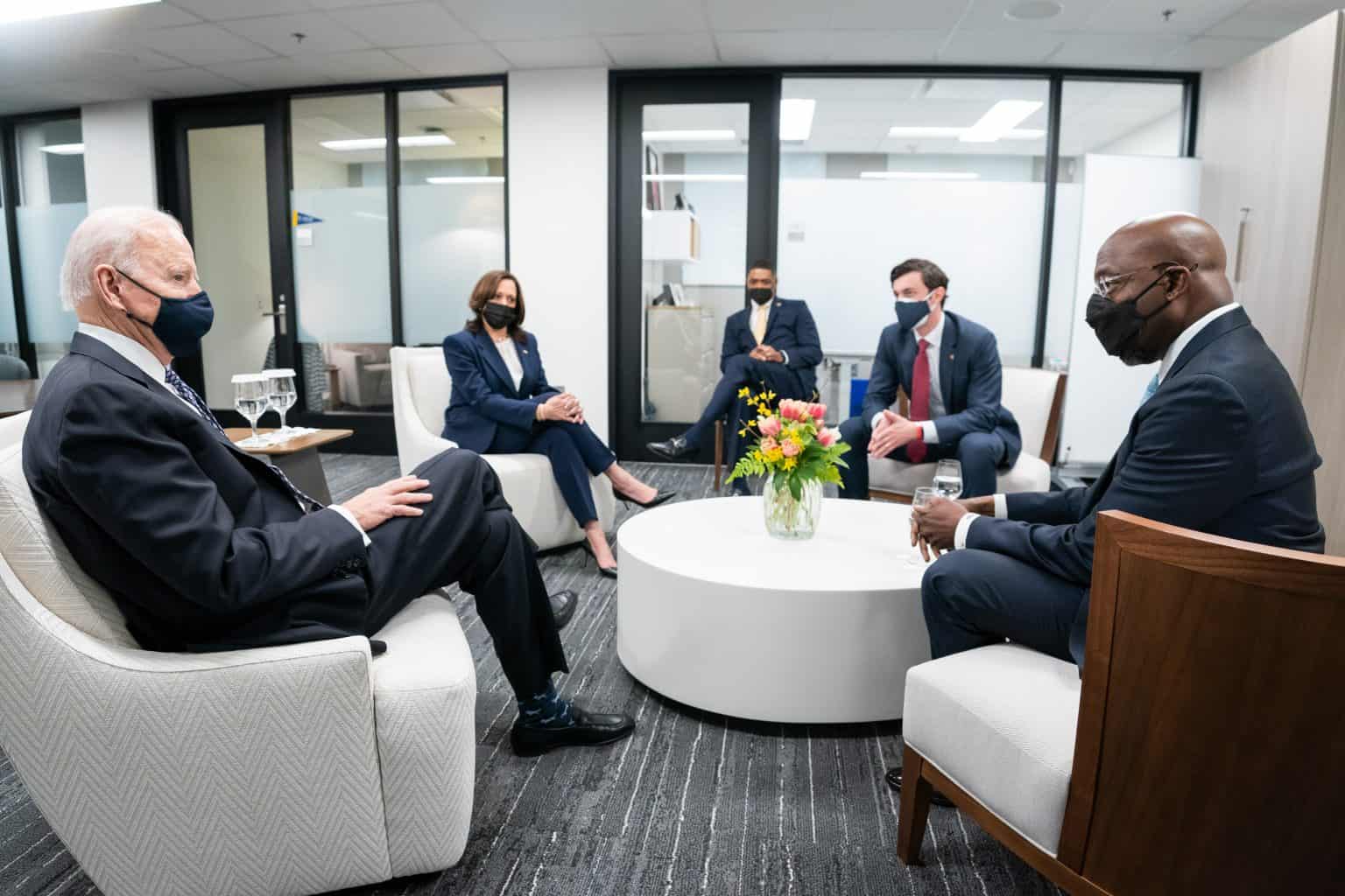 President Joe Biden, Vice President Kamala Harris, Senator Jon Ossoff, and Senator Reverend Raphael Warnock having a discussion around a white circular table with flowers in a vase.